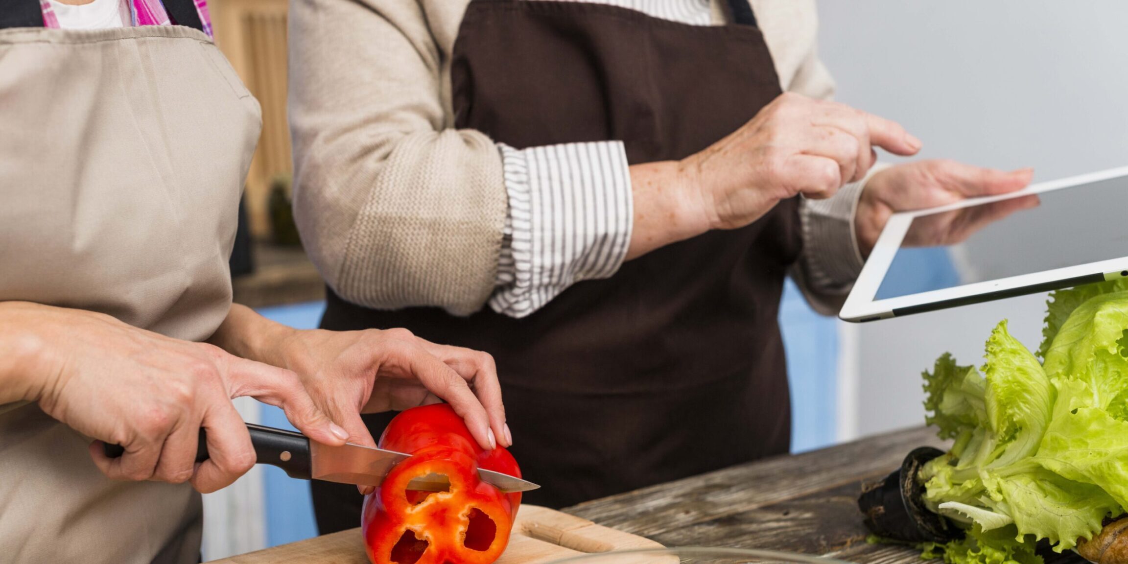 close-up-daughter-standing-with-her-mother-holding-digital-tablet-cutting-bell-pepper-with-knife
